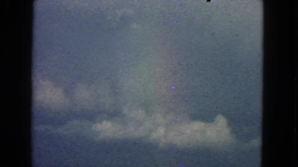 1963 San Francisco 8mm frame showing puffy clouds low in the sky, a faint rainbow tint, grain, and dark film edges.