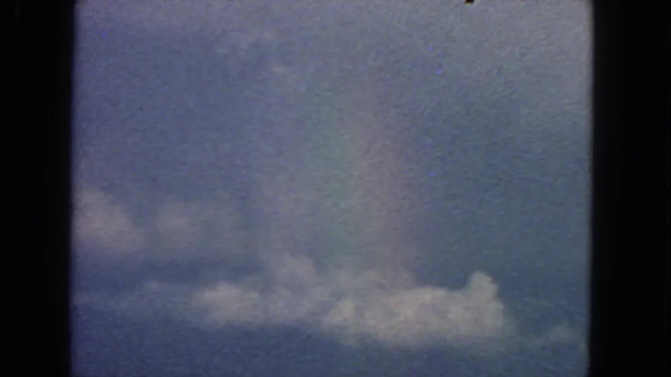 1963 8mm airplane-window view near San Francisco showing blue sky, a horizontal cloud bank, dark frame edges, and film grain.