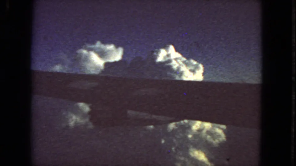1963 8mm airplane-window footage near San Francisco showing bright cloud tops below a dark horizon band and grainy blue-purple sky.