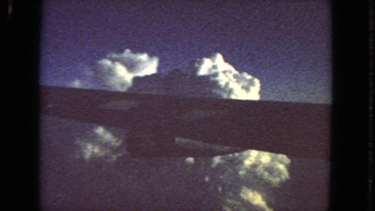 1963 8mm passenger view near San Francisco metadata, showing clouds beyond a dark aircraft wing or window edge.