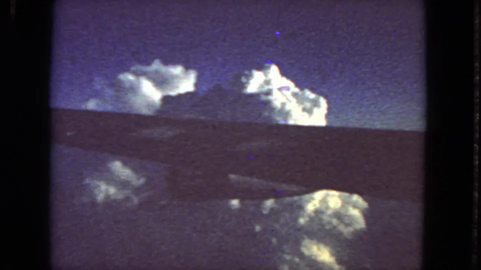 Grainy 8mm in-flight view with cloud formations, a dark aircraft edge, and purple-blue sky from the 1963 San Francisco clip metadata.