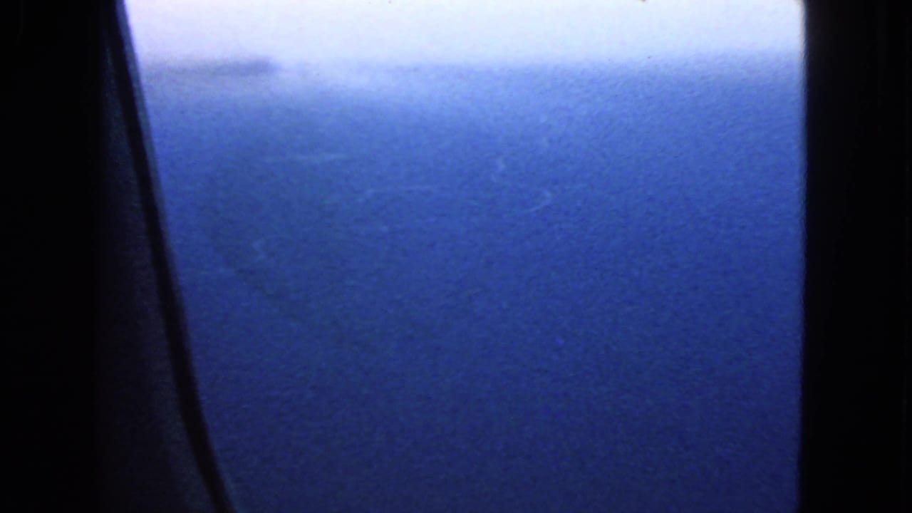 Deep blue ocean below a pale horizon, divided by dark airplane window framing.
