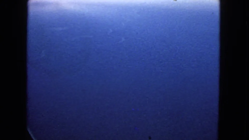Close aerial view of blue ocean from an airplane window in 1963 home-movie footage, with grain and dark framing visible.