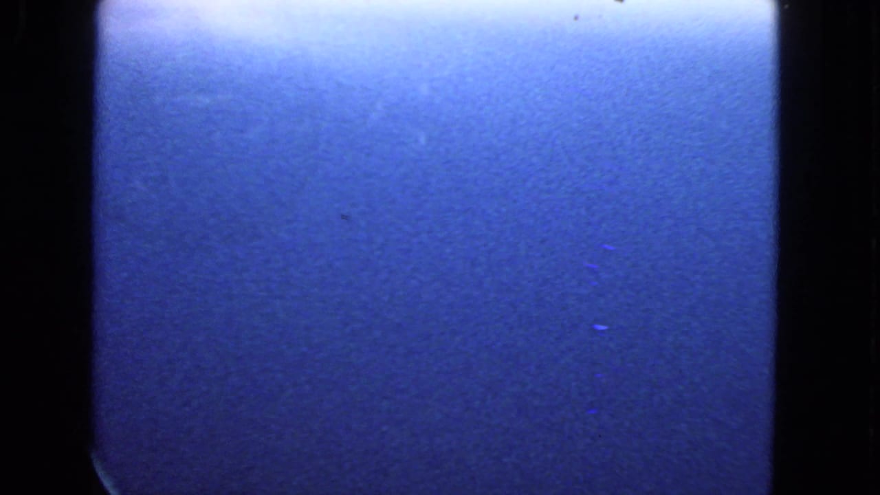 1963 8mm frame from a passenger-window view, dominated by blue sky and dark window edges with soft grain.
