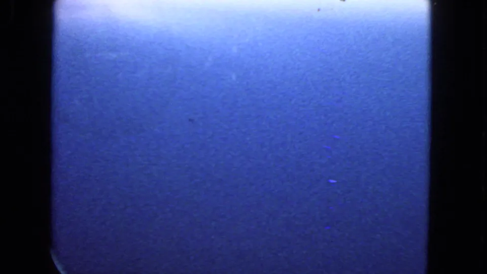 1963 8mm frame from a passenger-window view, dominated by blue sky and dark window edges with soft grain.