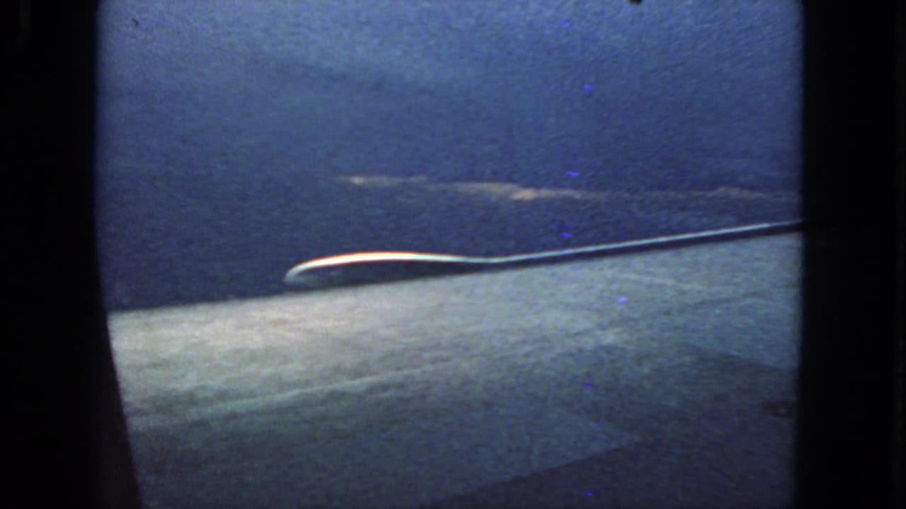 Airplane window view with blue sky and a pale wing-like aircraft surface.