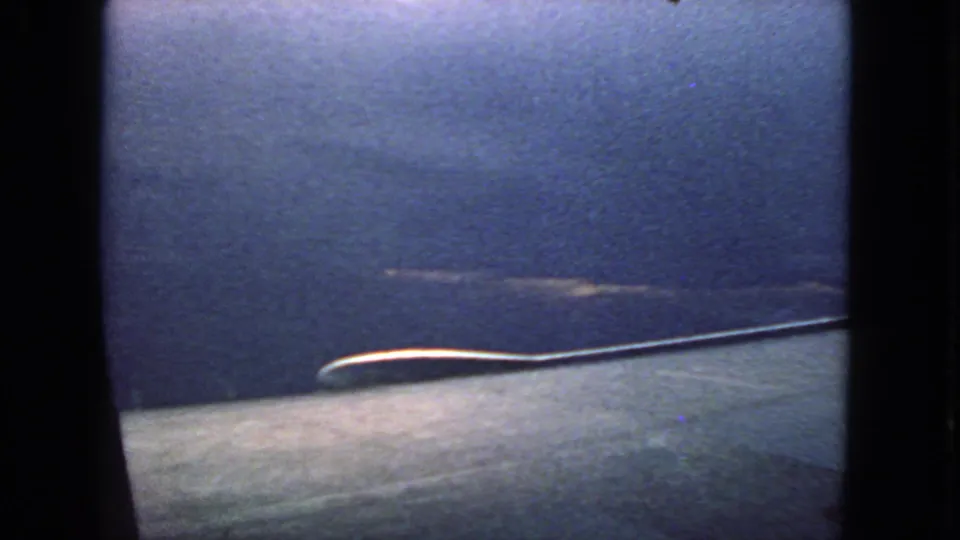 End frame of a 1963 8mm airplane-window view, with blue sky, a pale wing-like surface, and visible grain and flicker.