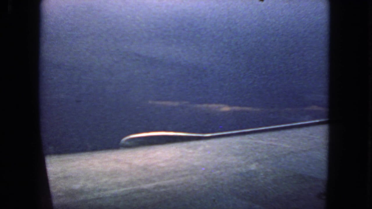 Dark blue sky seen through a rounded airplane window with faint cloud streaks and black film borders.