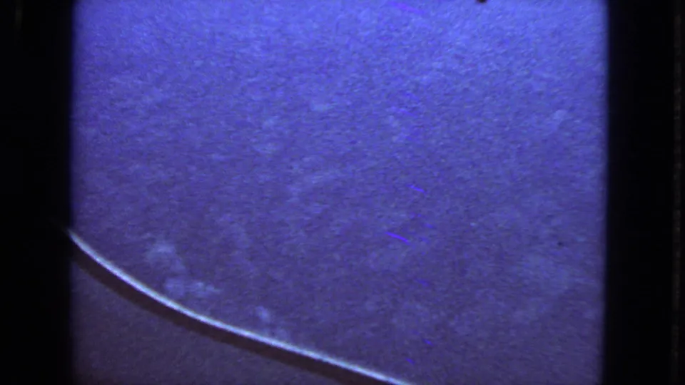 Blue-tinted 8mm frame from the 1963 flight view, showing haze or cloud texture and the lower curve of the airplane window.