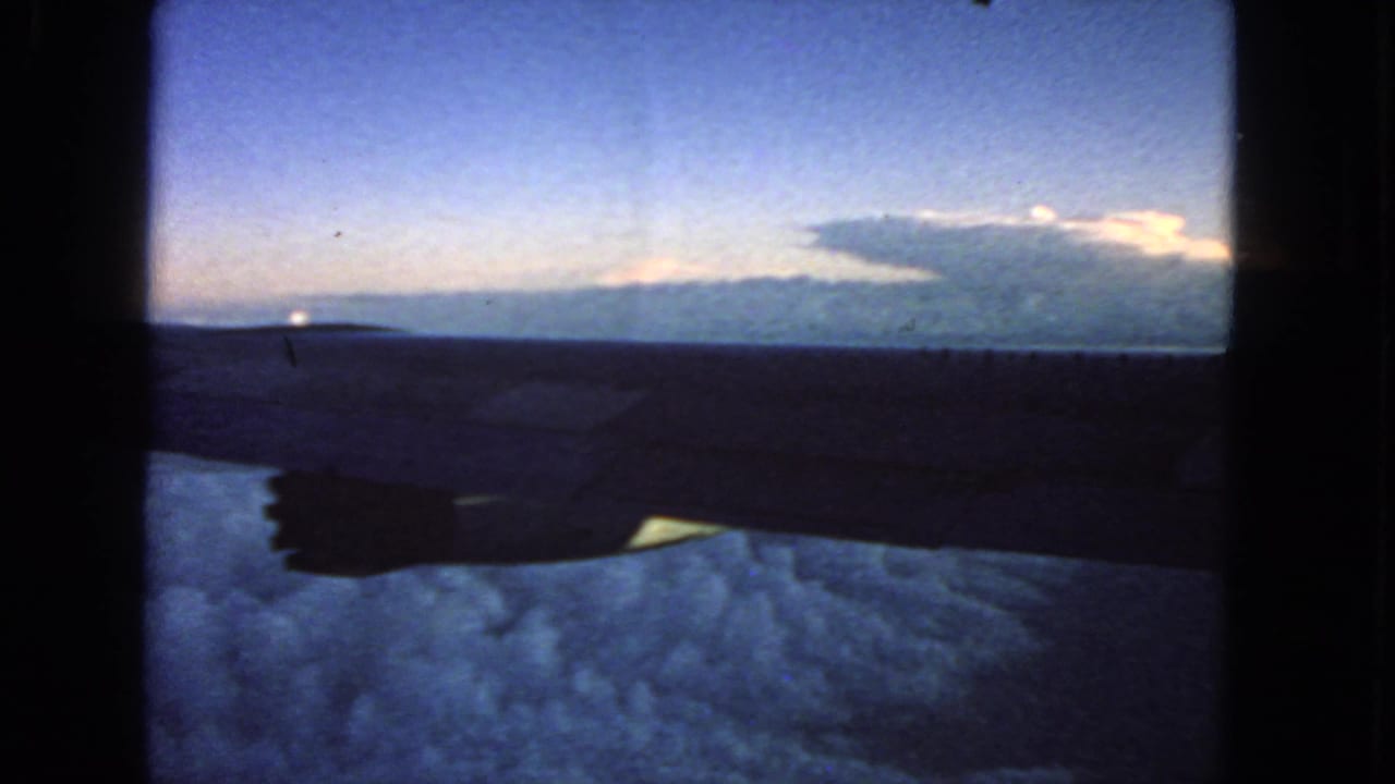 Airplane wing silhouetted above clouds beneath a blue dusk sky.