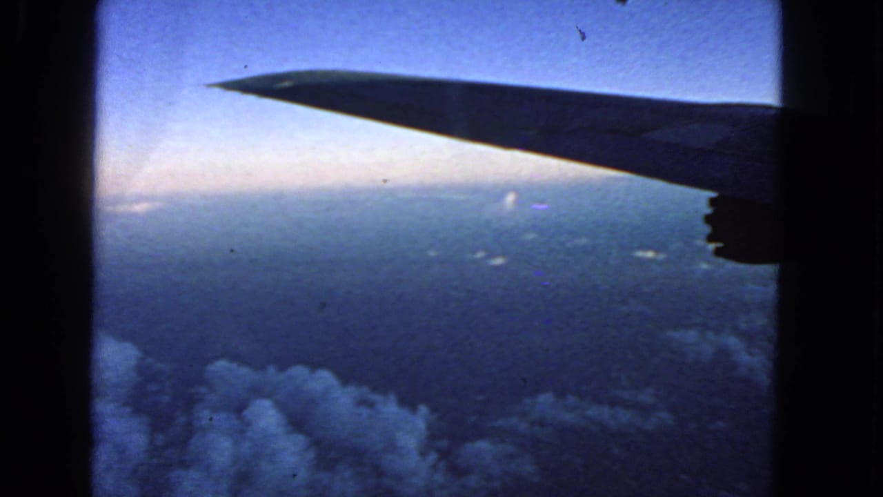 Dark airplane wing above clouds and distant horizon seen through a window.