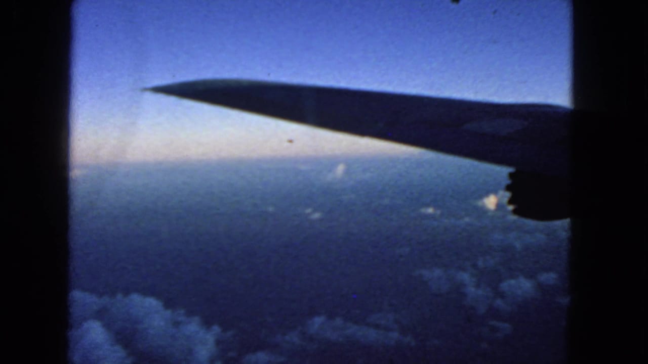 Dark airplane wing and engine silhouette above clouds and blue horizon.