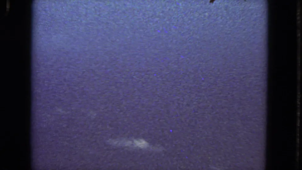 Soft 1963 8mm aerial view with a small pale cloud patch against blue haze from the passenger-window perspective.
