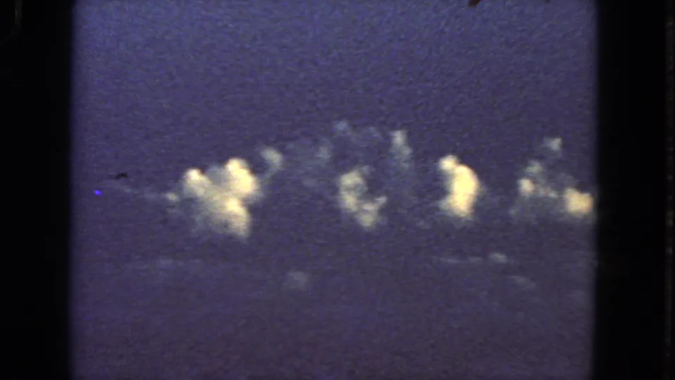 Blue-toned 8mm frame showing bright cloud clusters below the aircraft during the 1963 passenger flight.