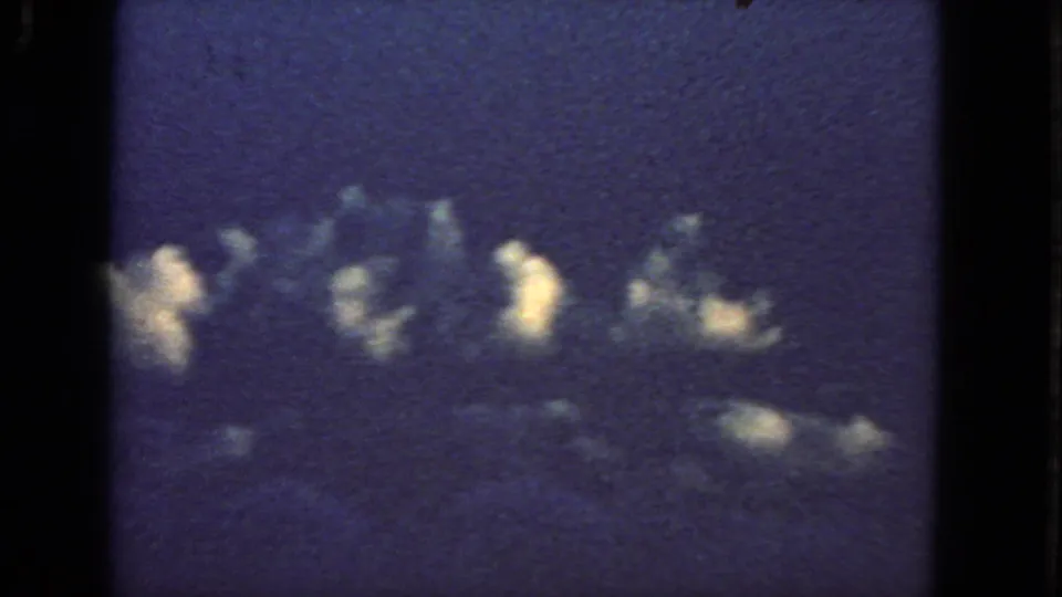 Aerial 8mm view from the 1963 clip, with cloud tops and multiple bright bursts visible through dark aircraft window framing.