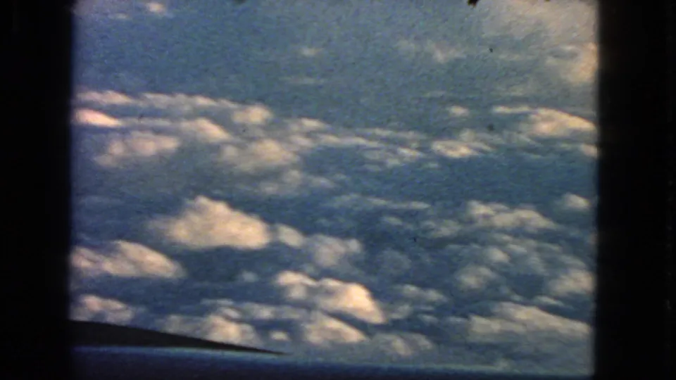 End frame from the 1963 8mm clip, showing a passenger-window view of clouds and sky with visible film grain and gate edges.