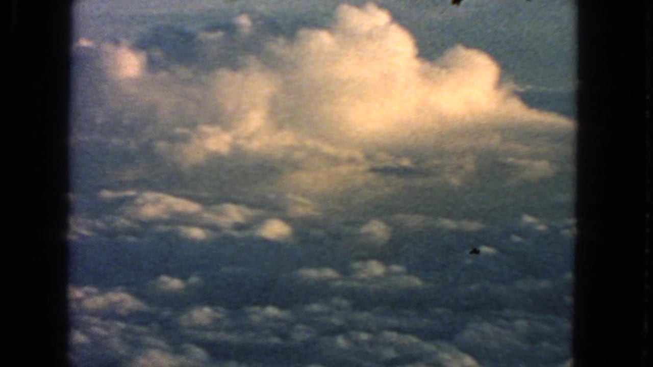 Sunlit cumulus cloud bank seen beyond dark airplane window framing.