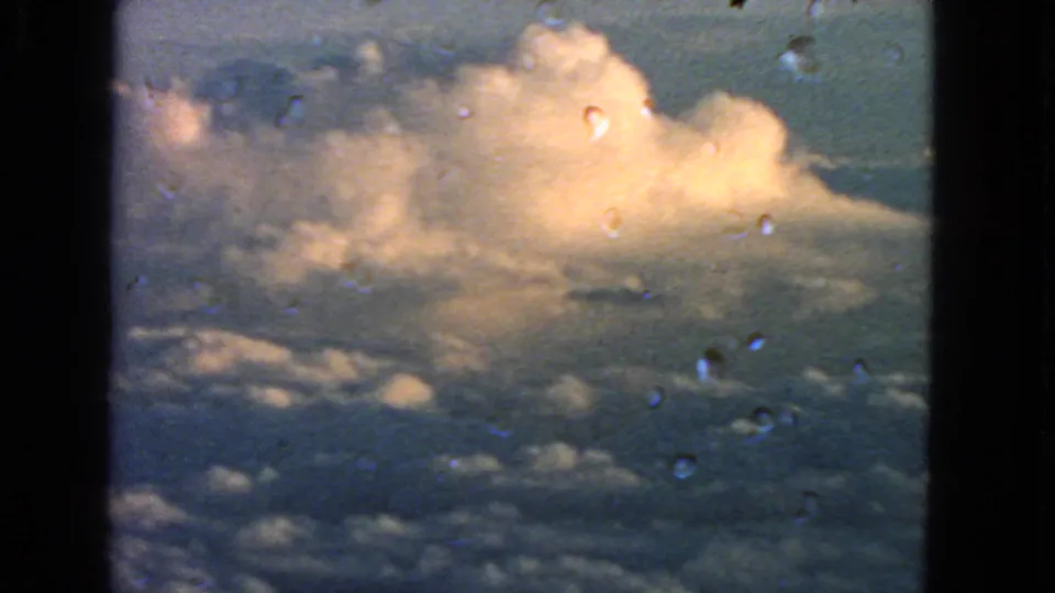 1963 8mm aerial view of a bright cumulus formation with visible film specks and window framing.