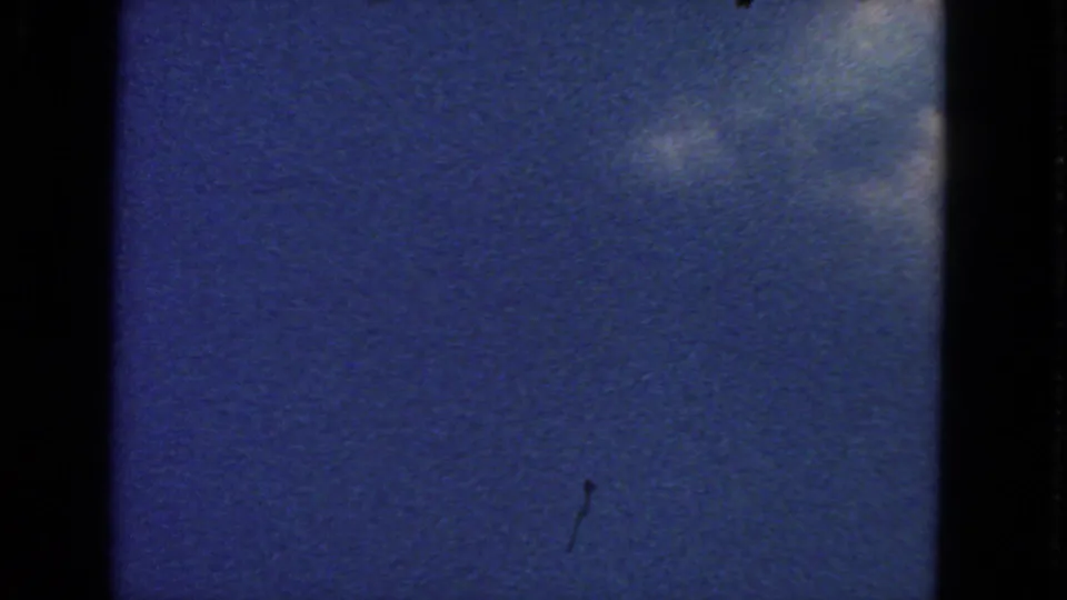 A sparse aerial sky view on 8mm film, showing blue sky, faint cloud texture, and dark vertical frame borders.