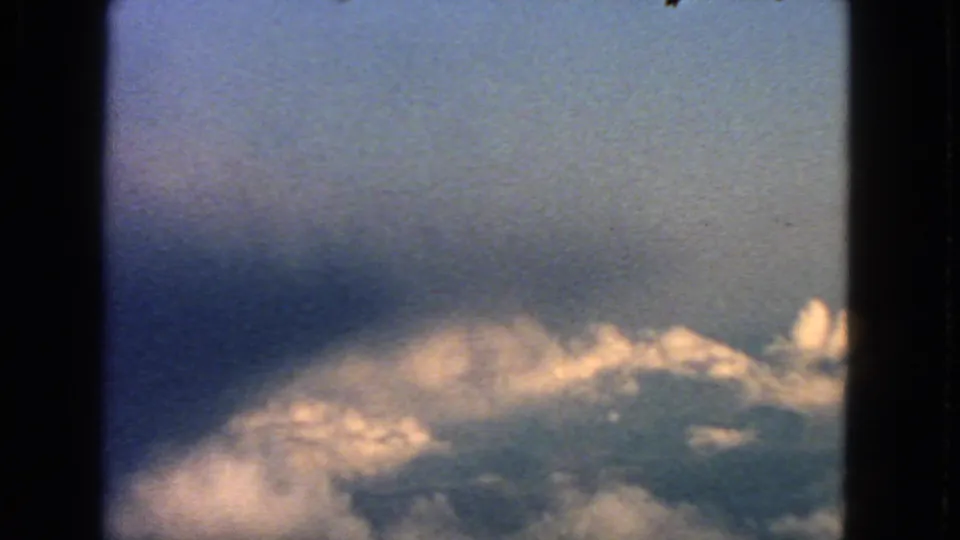 8mm aerial cloudscape from 1963, with warm cloud highlights at the bottom and soft blue sky above.