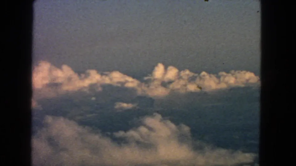 Aerial 8mm view from a passenger window, with sunlit cloud banks stretching across the frame.