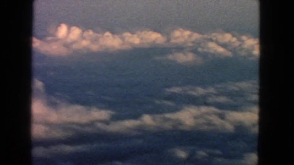 A 1963 8mm airplane-window view with dark frame edges, blue sky, and clouds below.