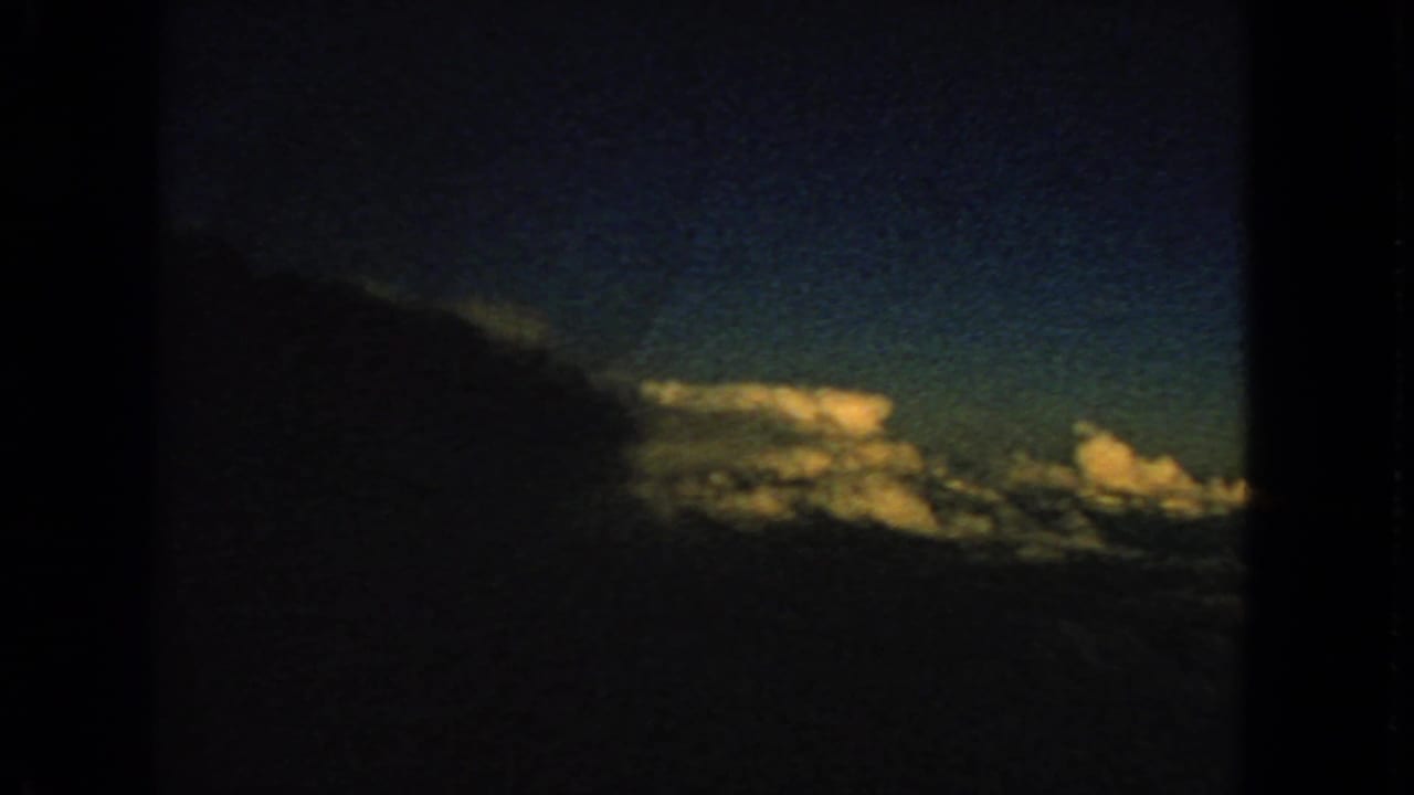 Dark airplane window framing blue sky and sunlit clouds.