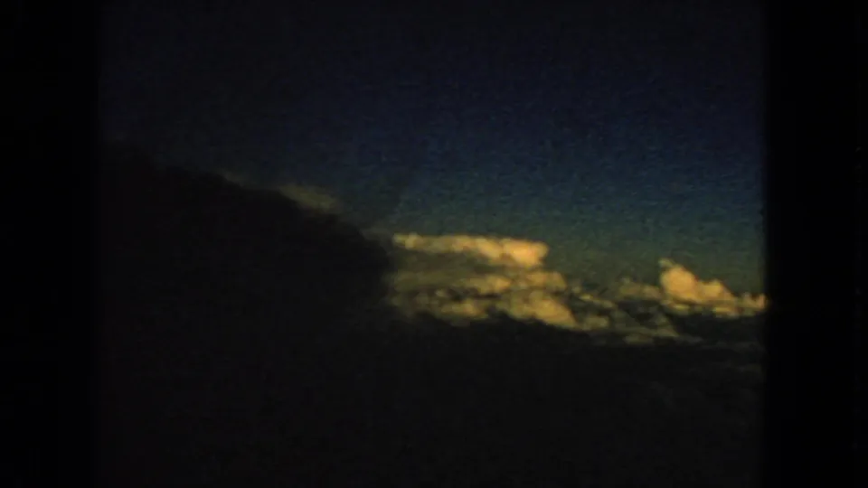 1963 8mm passenger-window view with dark aircraft framing, blue sky, and bright cloud tops.