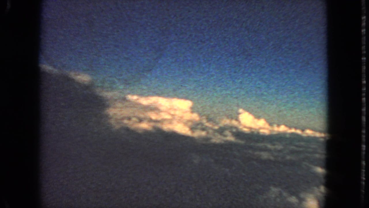1963 8mm home-movie view of blue sky and bright cloud tops from an airplane-window perspective.