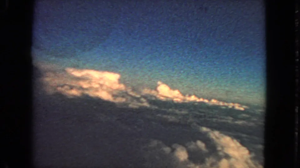 1963 archival home-movie frame showing a tilted aerial cloud view through an airplane window.