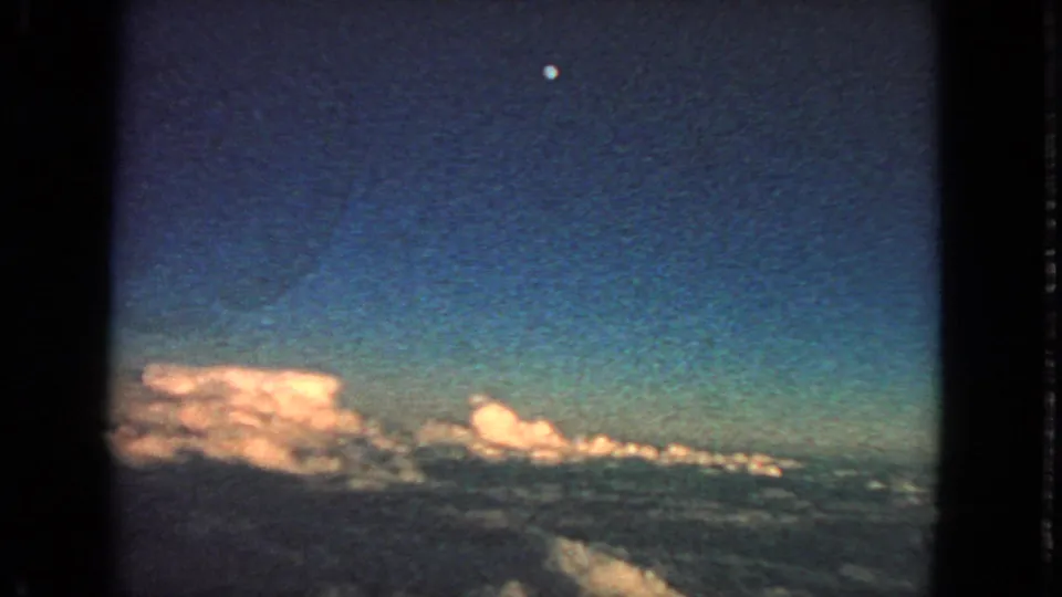 1963 8mm high-altitude passenger view showing cloud banks, deep blue sky, and a small moon, with film edges visible.