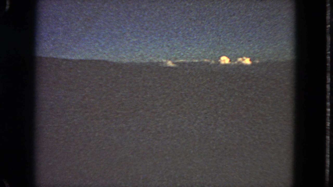 1963 8mm night view, likely near San Francisco, with faint lights along a dark horizon and a dim blue-black sky.