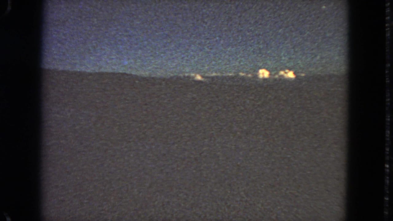 Faint night horizon with scattered lights and dark film borders.