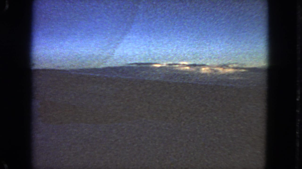 Aircraft-window view of blue sky, dark horizon, and dim terrain or water below.