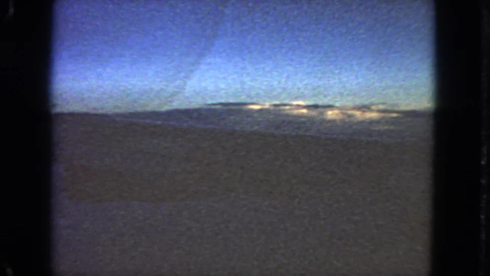1963 8mm aircraft-window view near San Francisco, with blue sky, distant horizon, and dark land or water below.