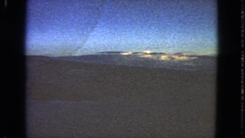 1963 8mm passenger view from an aircraft window, showing a blue sky and bright cloud bank near the horizon.