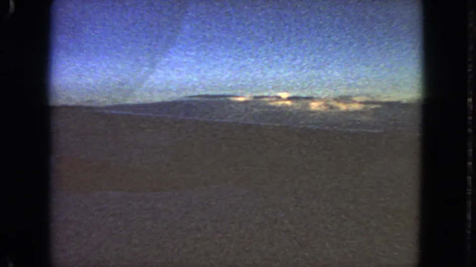 1963 8mm aircraft-window footage near San Francisco, with an indistinct horizon, pale sky, and dark ground or water below.