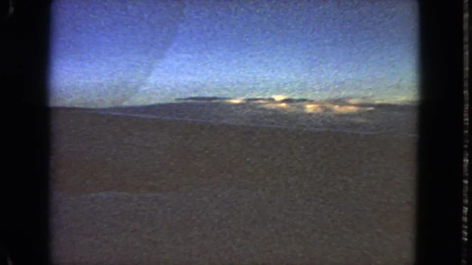 1963 8mm passenger-window view near San Francisco, with blue sky, distant light on clouds, and dark terrain or water below.