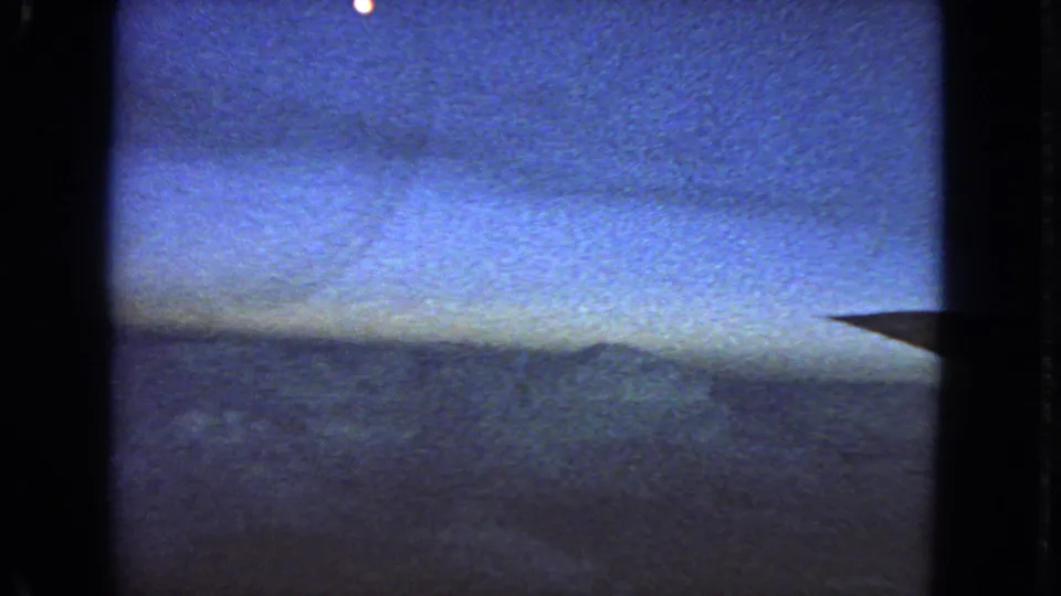 1963 8mm aerial view near San Francisco with blue dusk sky, soft clouds, and a dark aircraft wing edge on the right.
