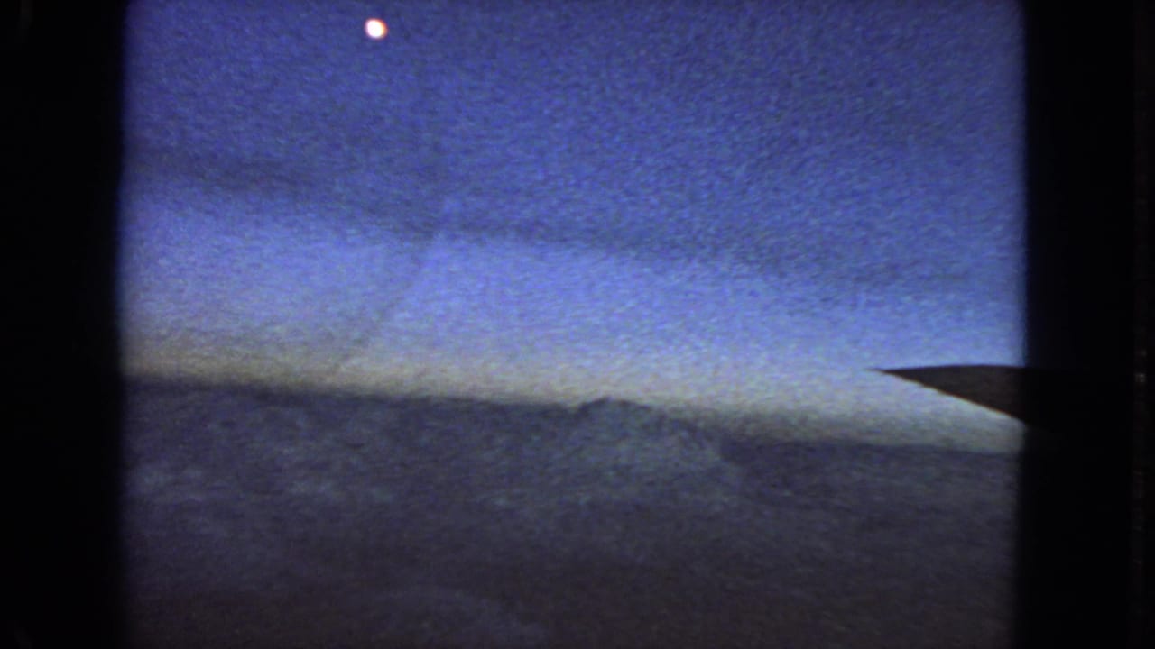 1963 8mm home-movie frame showing a blue twilight sky, a dark horizon or cloud band, and a small bright moon or planet near the top.