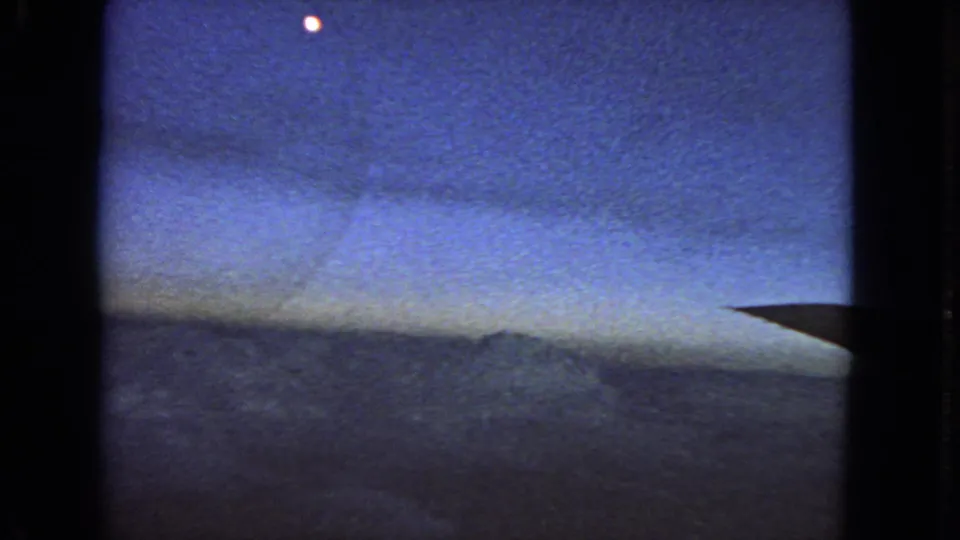 1963 8mm home-movie frame showing a blue twilight sky, a dark horizon or cloud band, and a small bright moon or planet near the top.