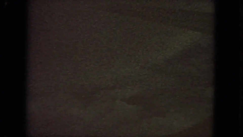 1963 8mm frame where a dark textured foreground or exposure shift fills most of the view beneath a narrow blue sky band.