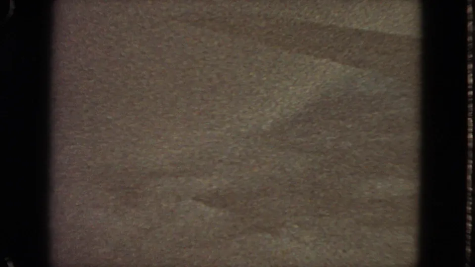 Final 1963 8mm frame showing a mostly dark, grainy surface with a faint blue horizon or exposure band across the top.