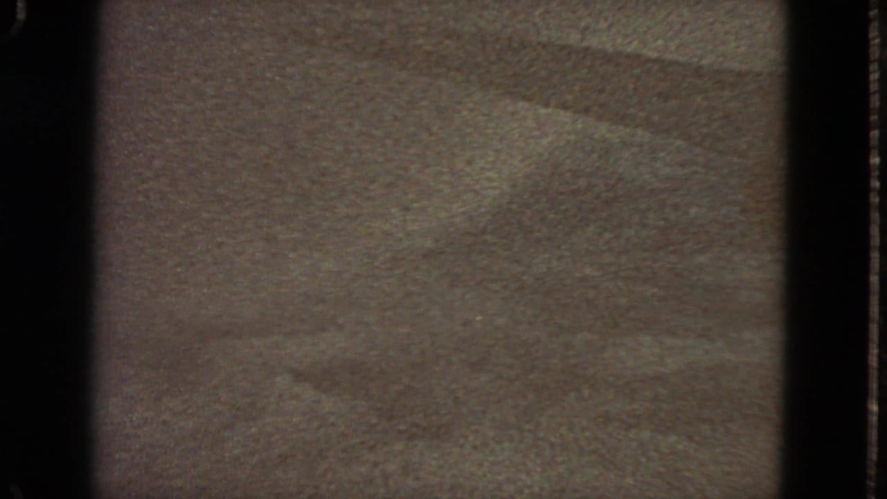 1963 8mm frame from San Francisco metadata showing a soft, grainy surface with faint diagonal shading and dark gate edges.
