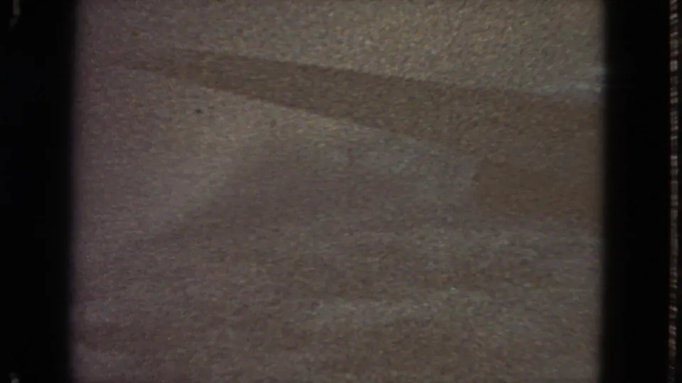 1963 8mm frame showing an abstract surface with a horizontal splice-like boundary, faint diagonal shading, and heavy grain.