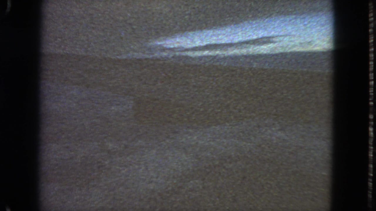 Dark car-window view with clouded sky, distant horizon, and visible film edges.