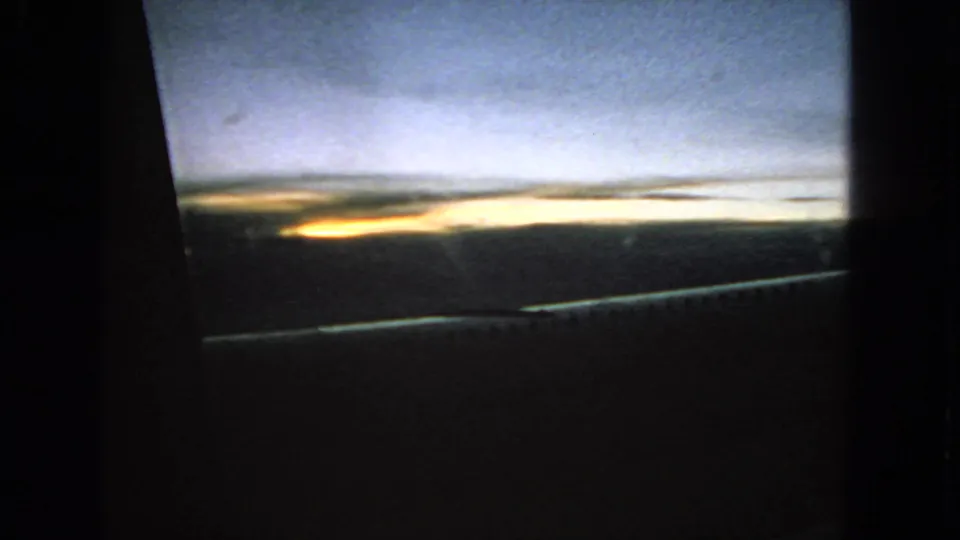 Archival 8mm frame showing a low yellow dawn glow, blue sky, and dark landscape through a window, consistent with supplied 1963 location metadata.