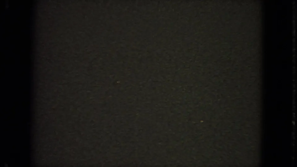 Dark, grainy 8mm end frame with minimal visible detail, likely leader or underexposed end-of-roll footage from the same clip.