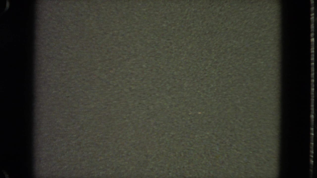 Low-light 1963 8mm San Francisco home-movie frame showing mostly dark olive-gray texture, grain, and film-edge shadows.