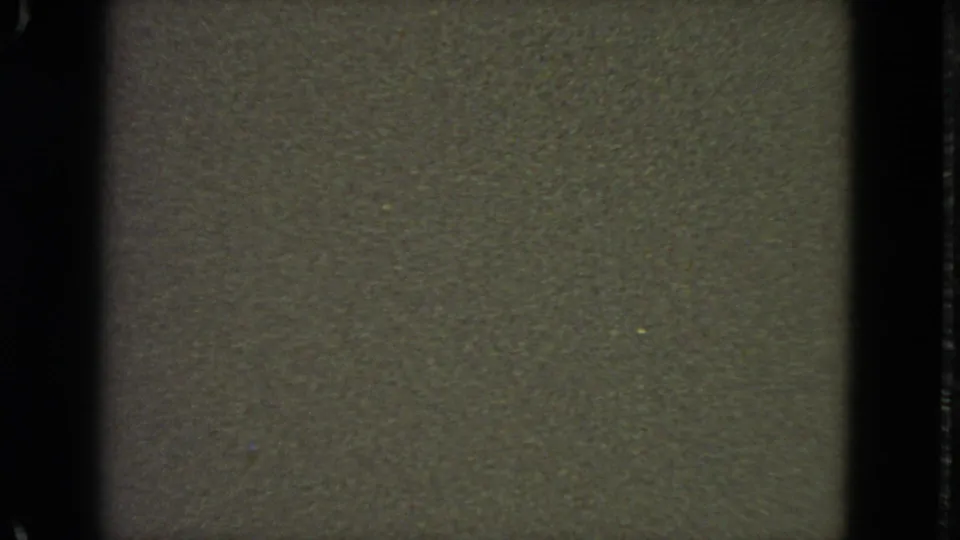 Low-light 1963 8mm San Francisco frame with dark texture, heavy grain, film-strip borders, and a small bluish dot.